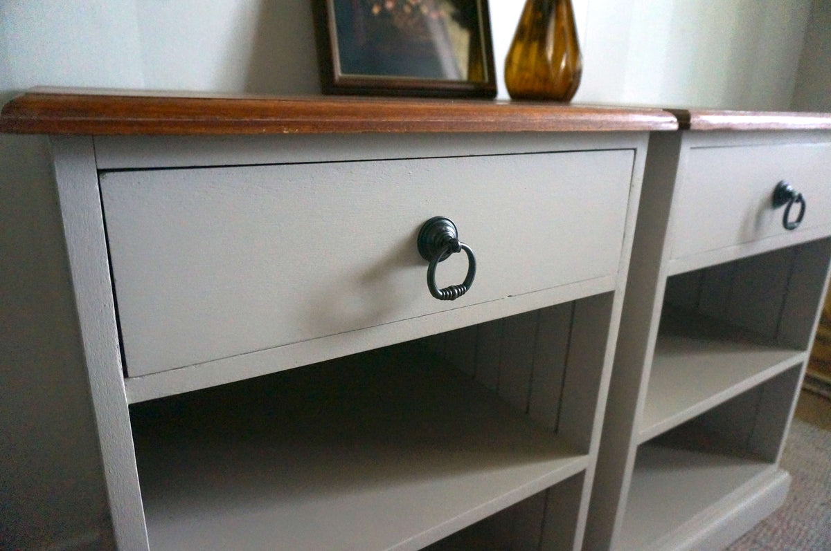 A close-up of a painted jarrah bedside table with a Velvet Taupe body, a medium brown wood top, and black metal drawer ring handles. A framed picture and an amber glass vase sit on top, and part of another matching cabinet is visible to the right.