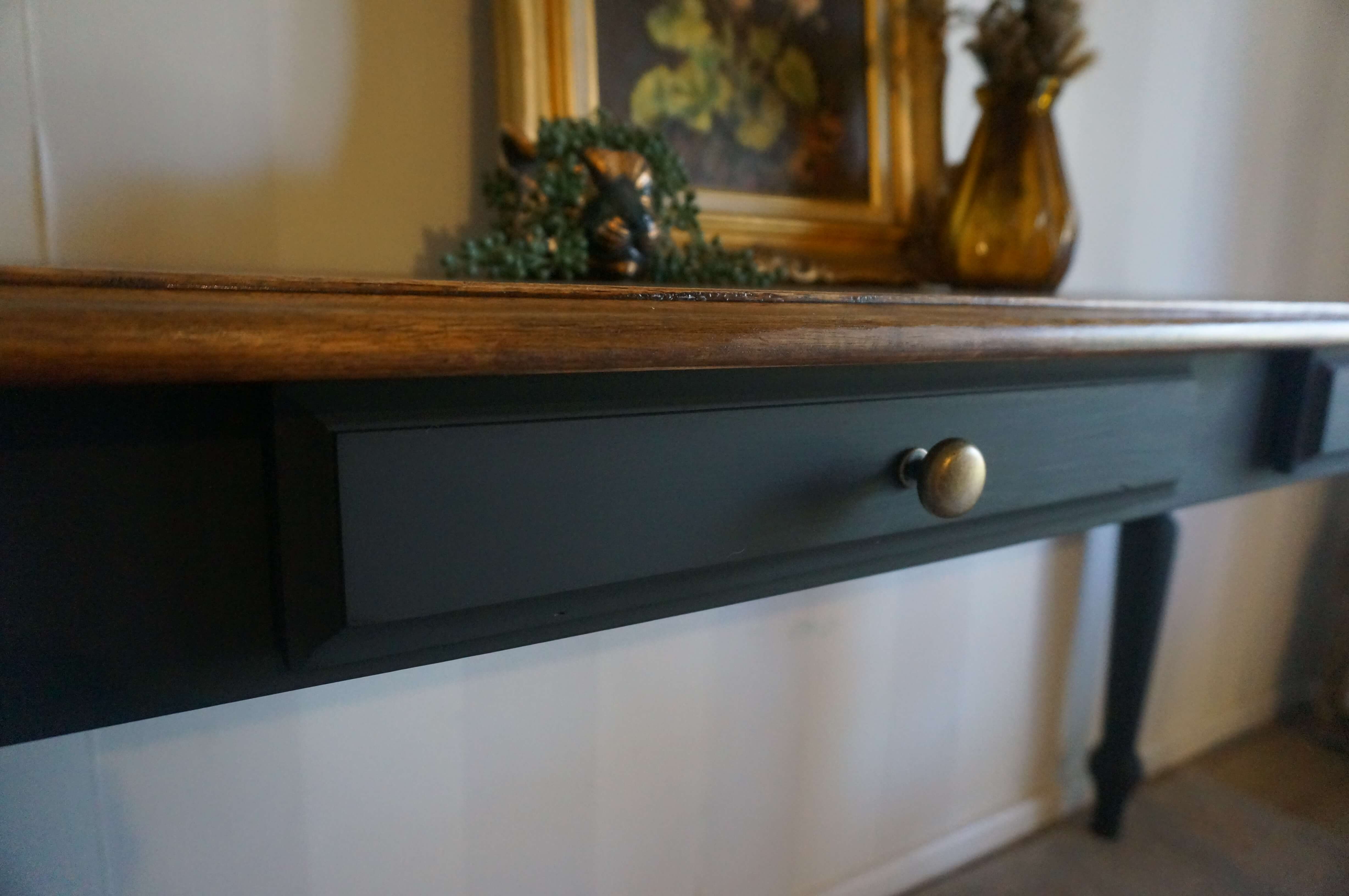 A close-up of a black vintage hall table drawer with a round brass knob, featuring a walnut wooden top and decorative items on top.