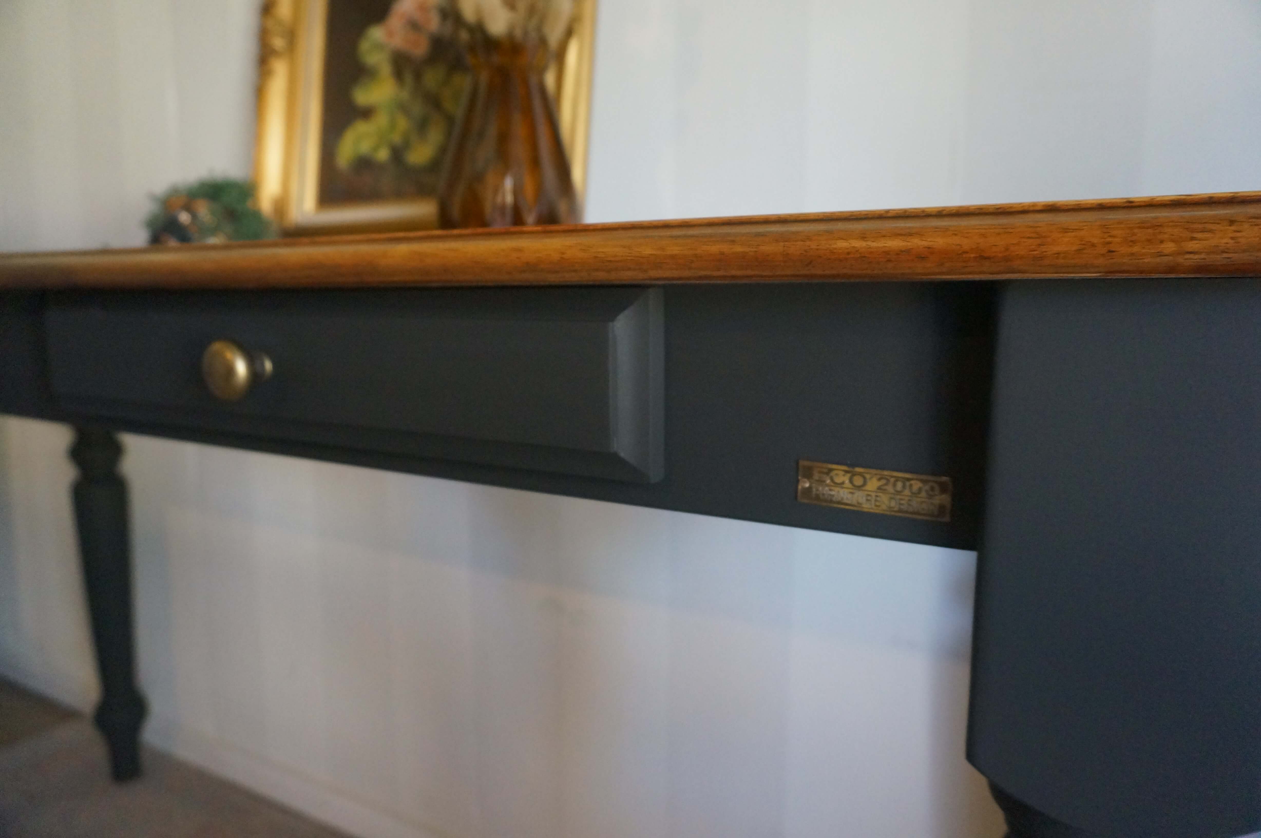 A close-up of a black painted hall table with a walnut wooden top, a single drawer with a brass knob, and a small brass plaque on the front.
