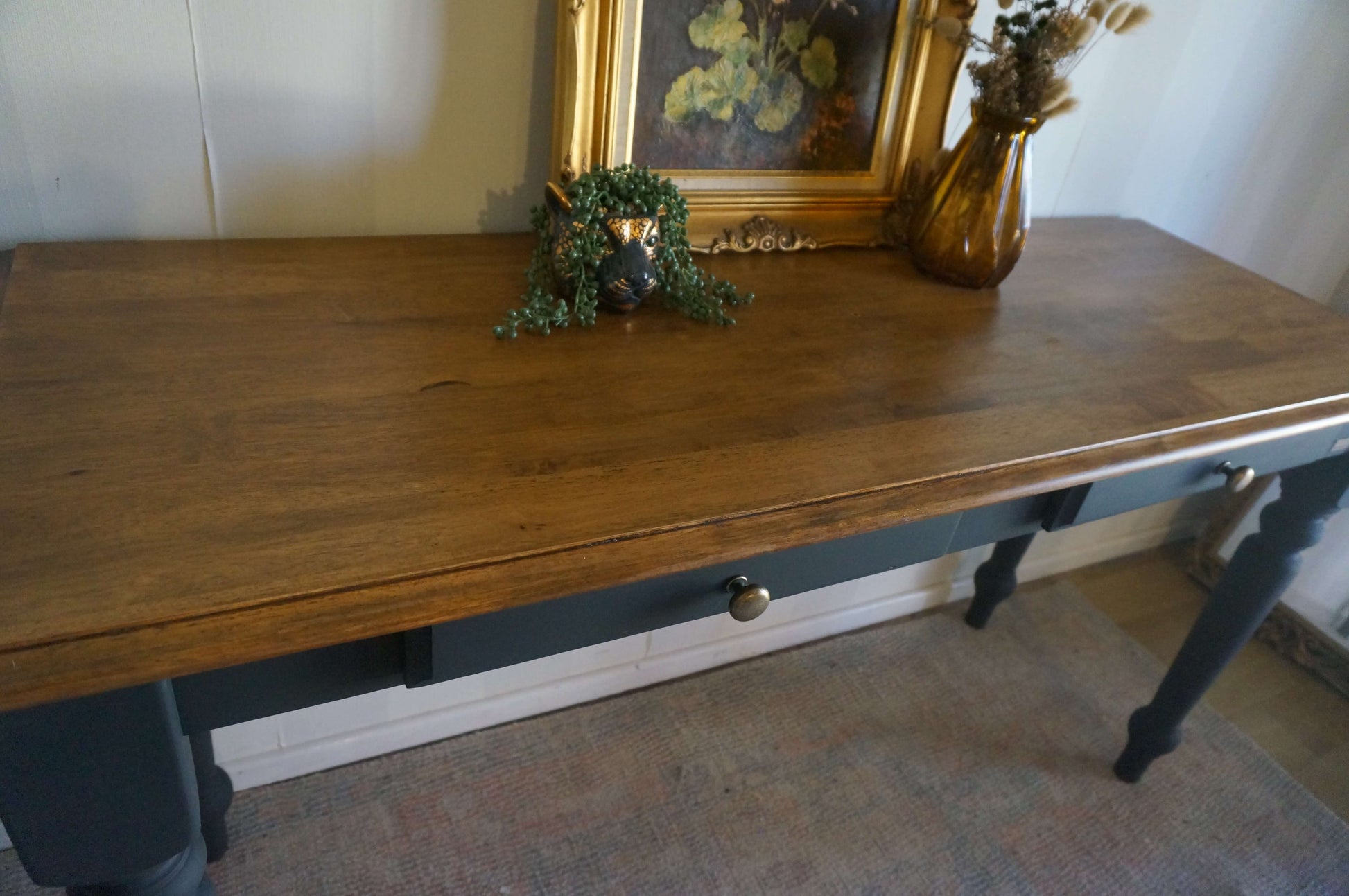 A vintage wooden hall table painting in black with a walnut brown wood top, styled with a small green plant and a gold-framed picture.