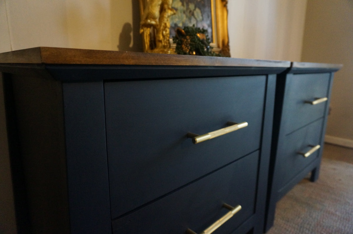 Dark navy blue wooden bedside tables with three drawers and gold metal handles, shown in a home setting.