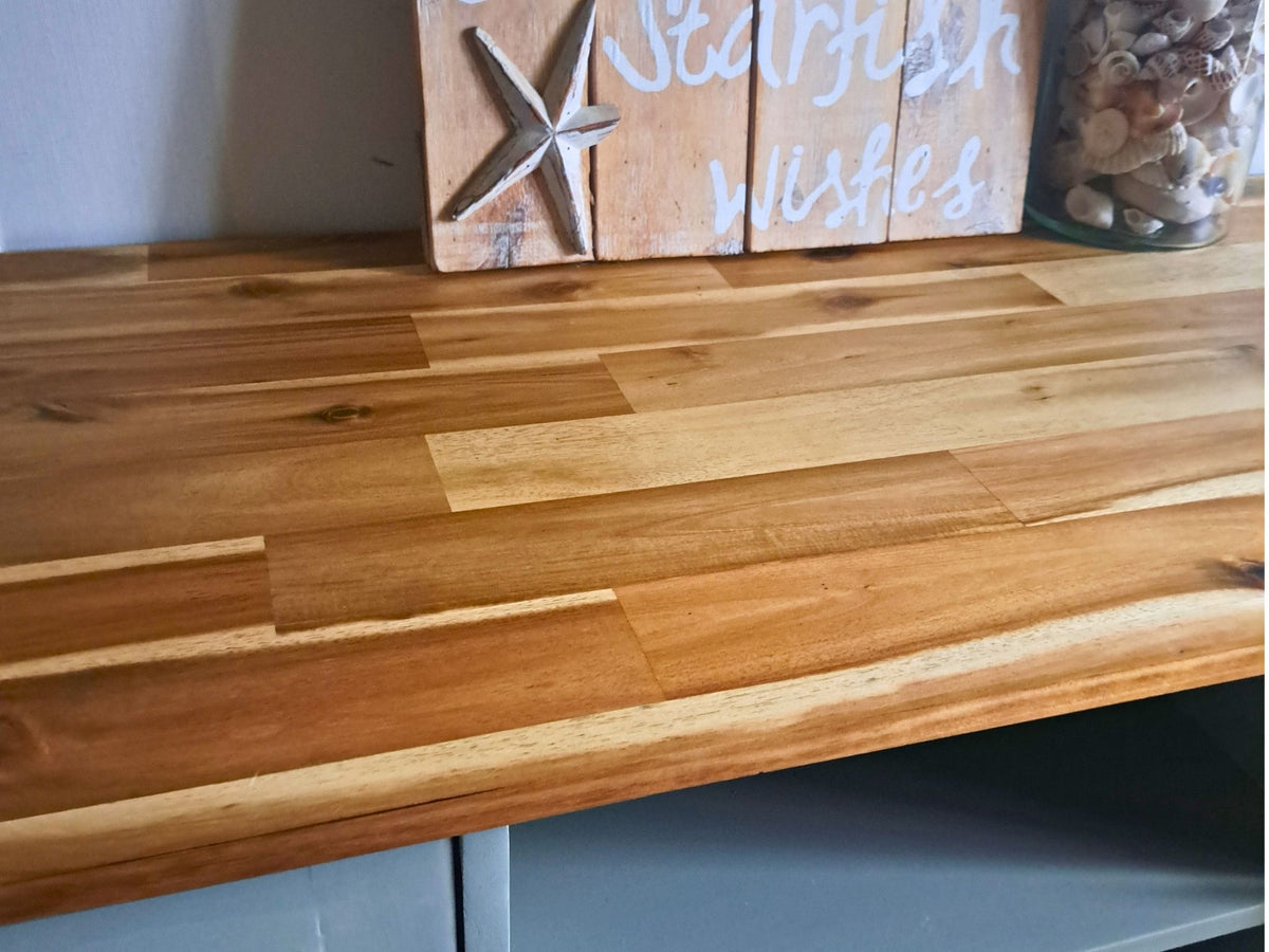 Natural timber detail on the Sage green TV unit. showing a close-up of the light brown wood with visible grain. There is a decorative wooden sign with a starfish and the words 'Starfish wishes' in the background. 