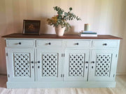A rustic sideboard cabinet painted in Willow with a dark brown wooden top, featuring four lattice-patterned doors and styled with a vase of eucalyptus, a candle, and books on a striped wall.